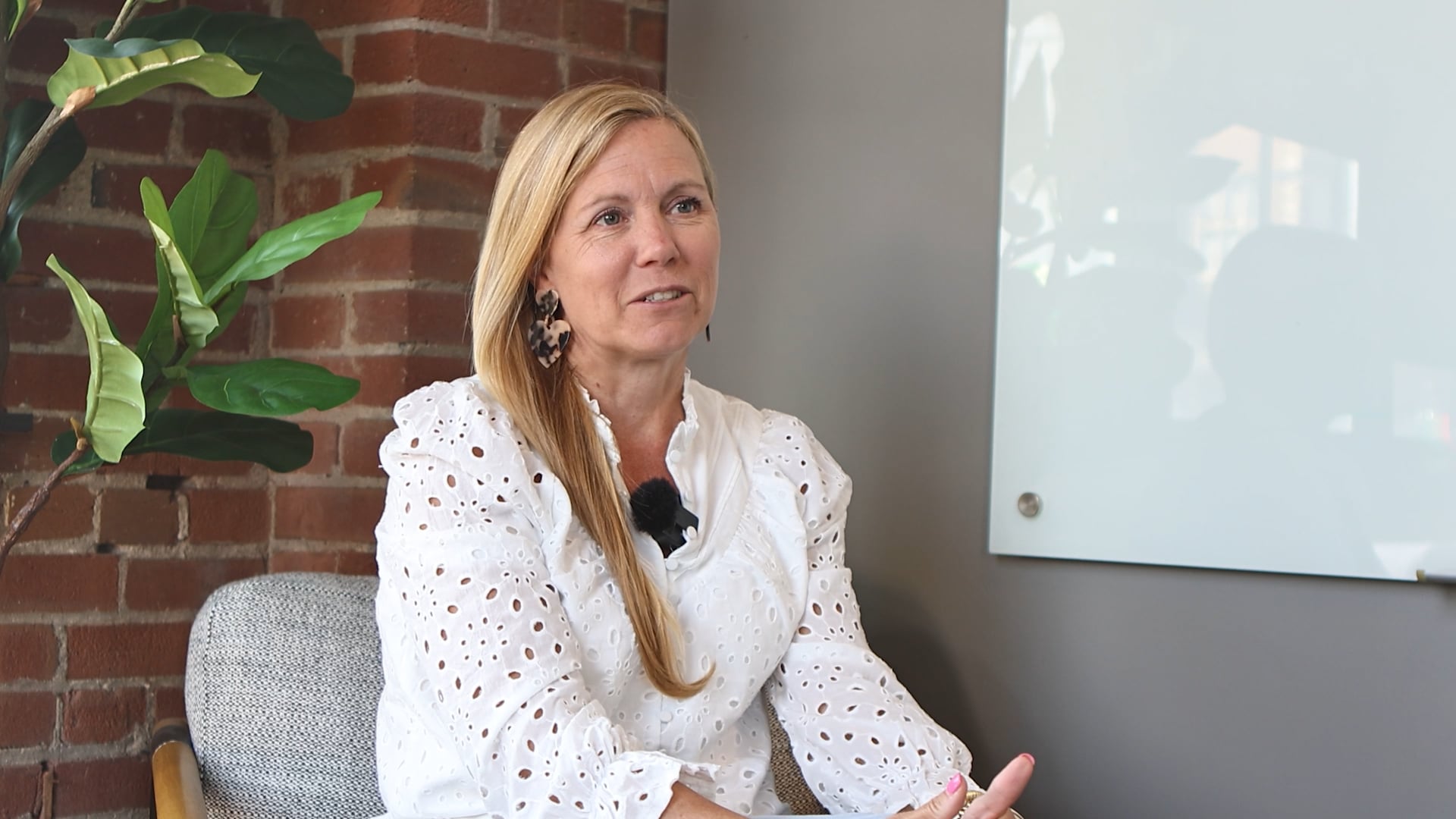 A blonde woman in a white shirt sitting in front of a brick wall
